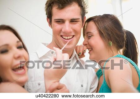 Stock Image - Teenage girls putting makeup on boy. Fotosearch