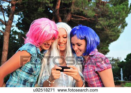 Stock Image - Teenage girls wearing colorful wigs. Fotosearch