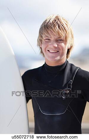 Stock Photo - Teenage surfer holding board on beach. Fotosearch