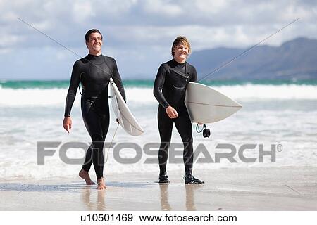 Teenage surfers carrying board on beach View Large Photo Image Stock Photo - Teenage surfers carrying board on beach. Fotosearch