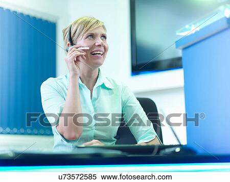 Stock Photography - Telephone receptionist using headset at desk. Fotosearch