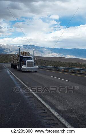 Stock Image - Truck carrying logs in rural landscape. Fotosearch