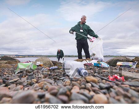 Stock Image - Two male environmentalists removing litter from seashore. Fotosearch