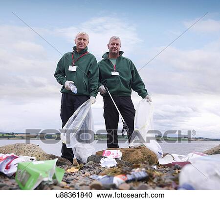 Stock Image - Two male environmentalists removing litter from seashore. Fotosearch