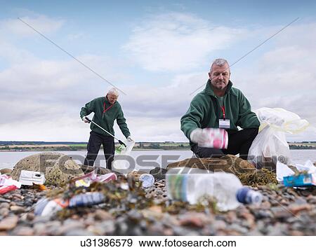 Two male environmentalists removing litter from seashore View Large Photo Image Stock Photo - Two male environmentalists removing litter from seashore. Fotosearch