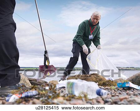 Stock Photography - Two male environmentalists removing litter from seashore. Fotosearch