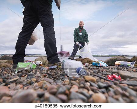 Stock Photography - Two male environmentalists removing litter from seashore. Fotosearch