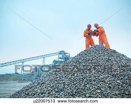 Stock Image - Two quarrymen inspecting stockpiles of quarried stone. Fotosearch