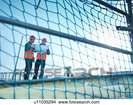 Picture - View through scaffolding of builders reading plans on factory roof. Fotosearch