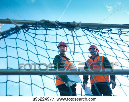 View through scaffolding of builders holding plans on factory roof View Large Photo Image Stock Photo - View through scaffolding of builders holding plans on factory roof. Fotosearch