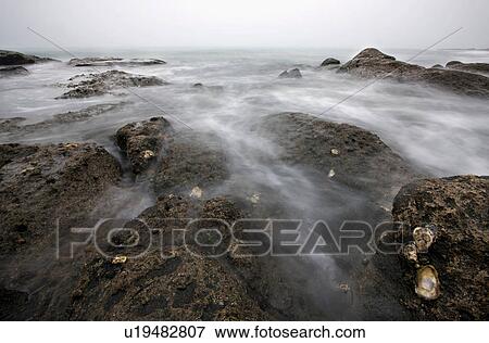 Stock Photo - Water washing over rocks on beach. Fotosearch