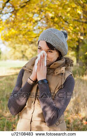 Stock Image - Woman blowing her nose in park. Fotosearch