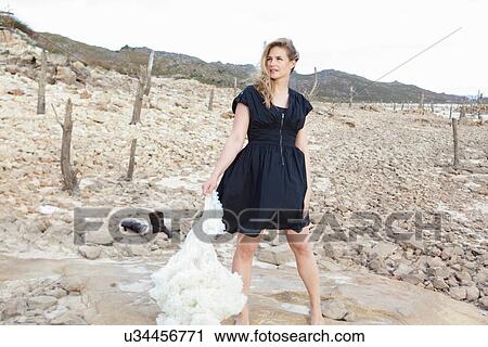 Stock Image - Woman carrying petticoat on rocky beach. Fotosearch