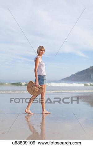 Stock Photo - Woman carrying straw hat on beach. Fotosearch