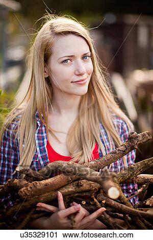 Stock Image - Woman gathering firewood in garden. Fotosearch