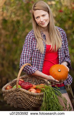 Stock Image - Woman gathering vegetables in garden. Fotosearch