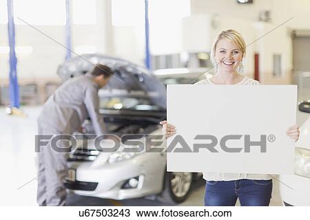 Stock Image - Woman holding blank card in garage. Fotosearch