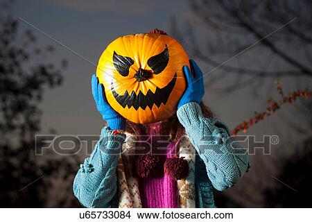 Woman holding jack o? lantern over face View Large Photo Image Picture - Woman holding jack o? lantern over face. Fotosearch