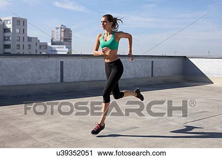 Stock Image - Woman jogging on rooftop. Fotosearch