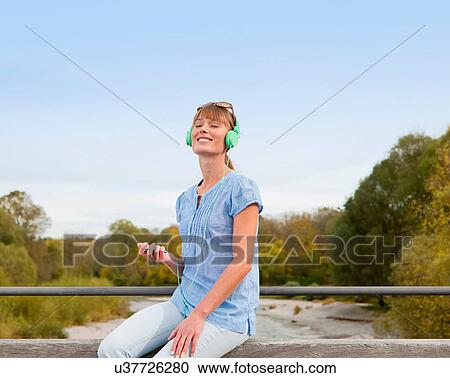 Stock Image - Woman listening to headphones outdoors. Fotosearch