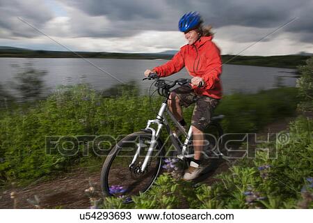 Stock Image - Woman mountain biking on dirt path. Fotosearch