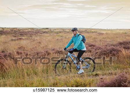 Stock Photography - Woman mountain biking on dirt path. Fotosearch