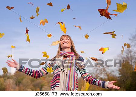 Stock Image - Woman playing in fall leaves. Fotosearch
