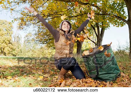 Stock Image - Woman playing with fall leaves in park. Fotosearch