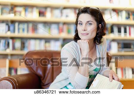 Stock Image - Woman reading book in library. Fotosearch