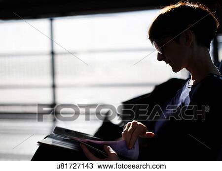 Stock Image - Woman reading magazine in airport. Fotosearch