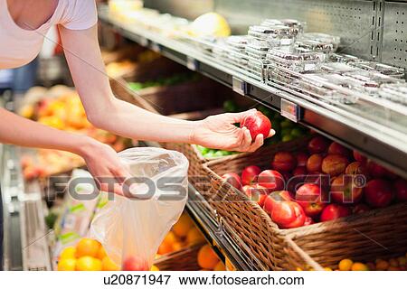 Stock Photo - Woman selecting fruit at grocery store. Fotosearch