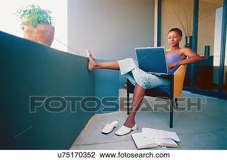 Stock Image - Woman using laptop in armchair. Fotosearch