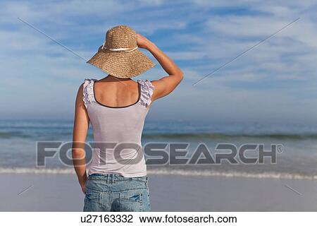 Stock Image - Woman wearing straw hat on beach. Fotosearch