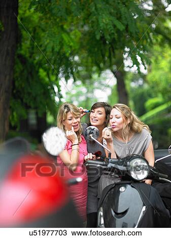 Stock Image - Women applying makeup in side mirror. Fotosearch