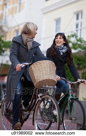 Women riding bicycles on city street View Large Photo Image Stock Image - Women riding bicycles on city street. Fotosearch