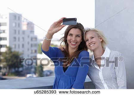Stock Image - Women taking picture on balcony. Fotosearch
