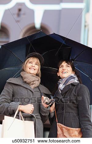 Stock Image - Women under umbrellas on city street. Fotosearch
