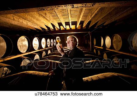 Stock Image - Worker testing whisky in distillery. Fotosearch