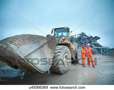 Workman driving industrial digger in quarry while colleagues conduct onsite meeting View Large Photo Image Stock Photo - Workman driving industrial digger in quarry while colleagues conduct onsite meeting. Fotosearch