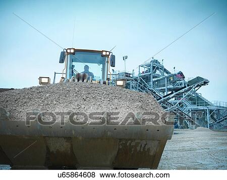 Stock Photo - Workman driving industrial digger on quarry site. Fotosearch