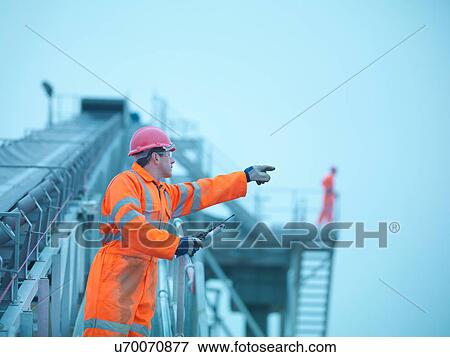 Workman in reflective clothing pointing from steps of screening conveyor at quarry View Large Photo Image Stock Photo - Workman in reflective clothing pointing from steps of screening conveyor at quarry. Fotosearch
