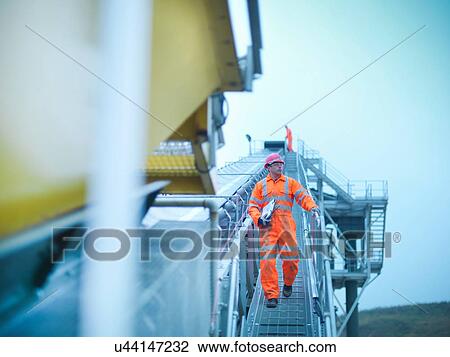 Stock Image - Workman in reflective clothing descending down steps of screening conveyor at quarry. Fotosearch