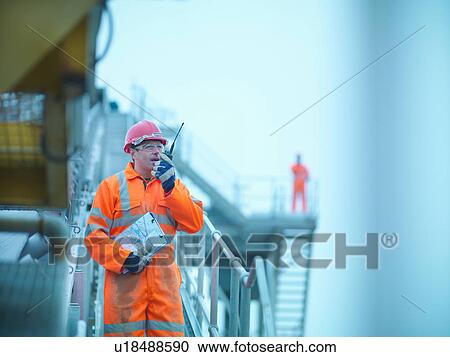 Stock Image - Workman in reflective clothing using walkie talkie to communicate to colleague at quarry. Fotosearch