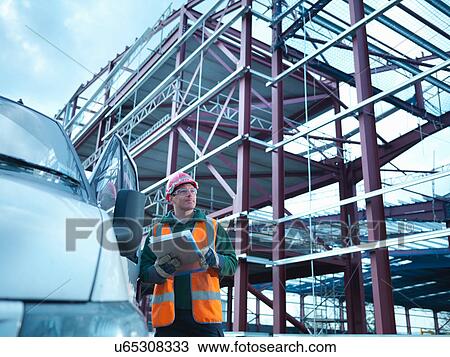 Workman looking up from clipboard by van and steel construction frame on building site View Large Photo Image Stock Image - Workman looking up from clipboard by van and steel construction frame on building site. Fotosearch