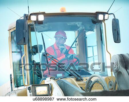 Stock Photo - Workman using walkie talkie in industrial digger on quarry site. Fotosearch