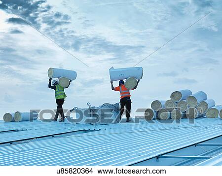 Workmen carrying rolls of insulation to install into factory roof View Large Photo Image Picture - Workmen carrying rolls of insulation to install into factory roof. Fotosearch
