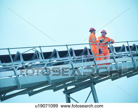 Stock Photo - Workmen in reflective clothing on steps of screening conveyor at quarry. Fotosearch