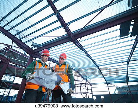 Stock Photo - Workmen looking at plans beneath steel construction frame on building site. Fotosearch