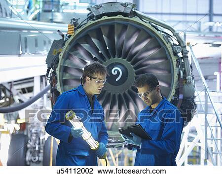Stock Image - Aircraft engineers discussing maintenance details on digital tablet in front of jet engine in aircraft maintenance factory. Fotosearch
