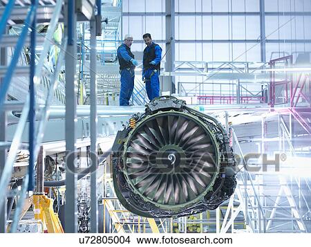 Picture - Aircraft engineers standing on wing with jet engine in aircraft maintenance factory. Fotosearch